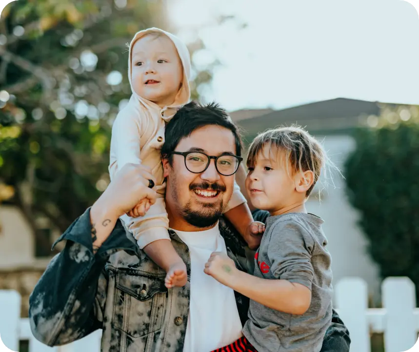 Foster parent holding children one on shoulders one in hands and smiling joyfully