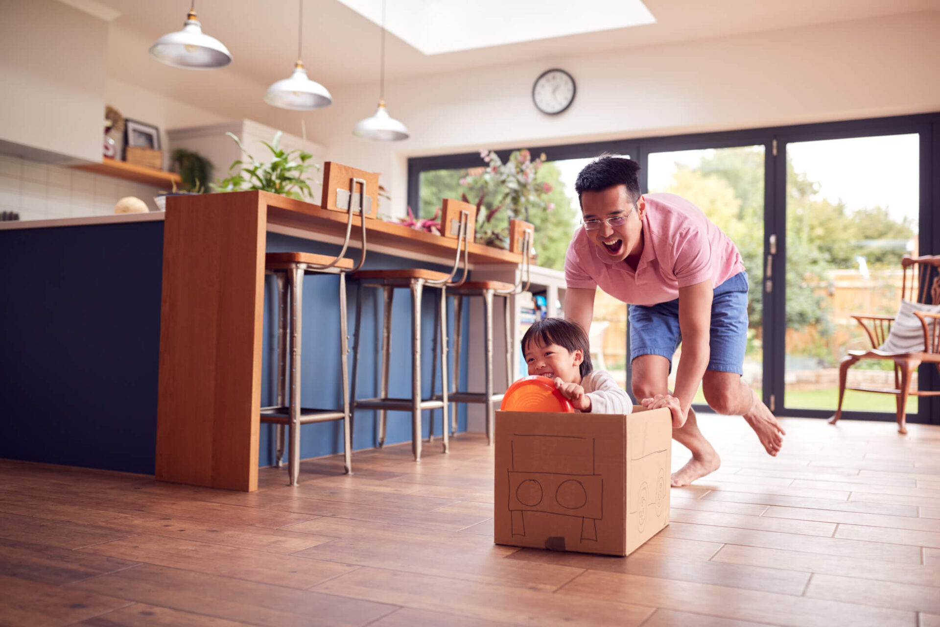 Foster parent and child pretending card board box is a car and driving it through the house