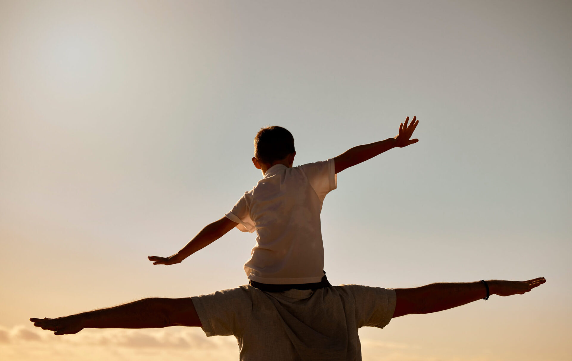 Child sitting on top of foster parents shoulders both extending hands to "fly".